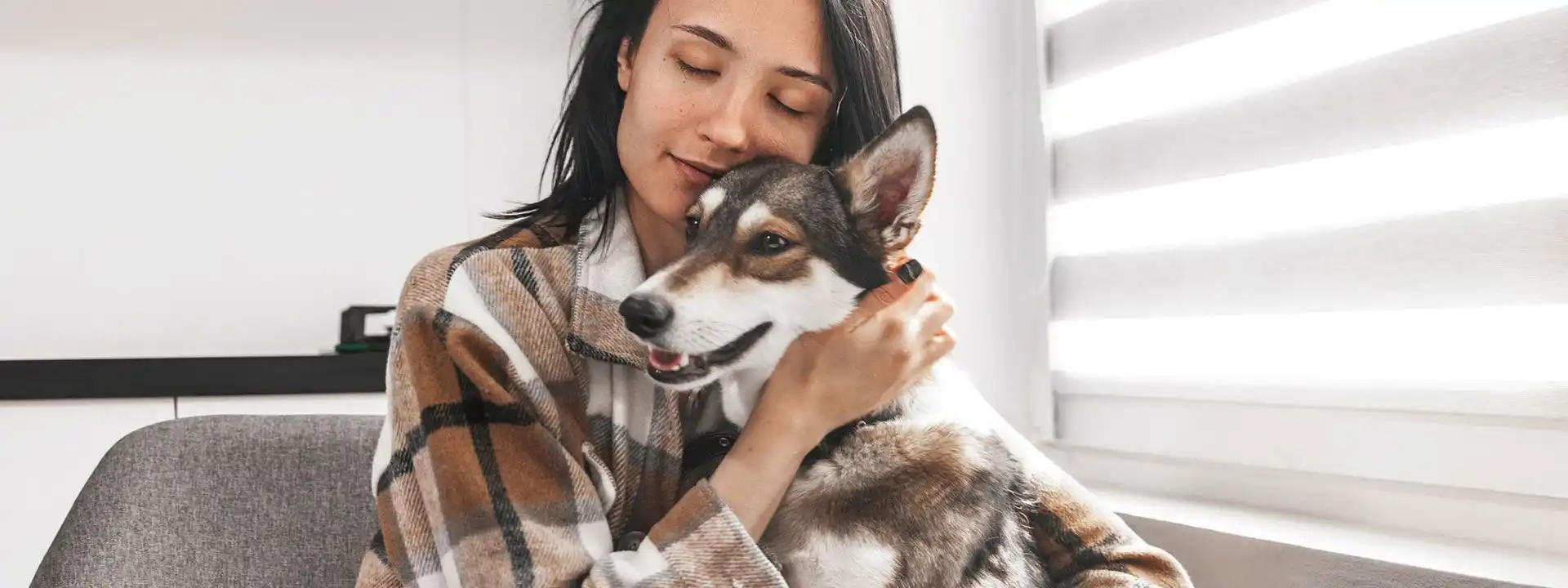 young woman hugging a dog seated near a bright window