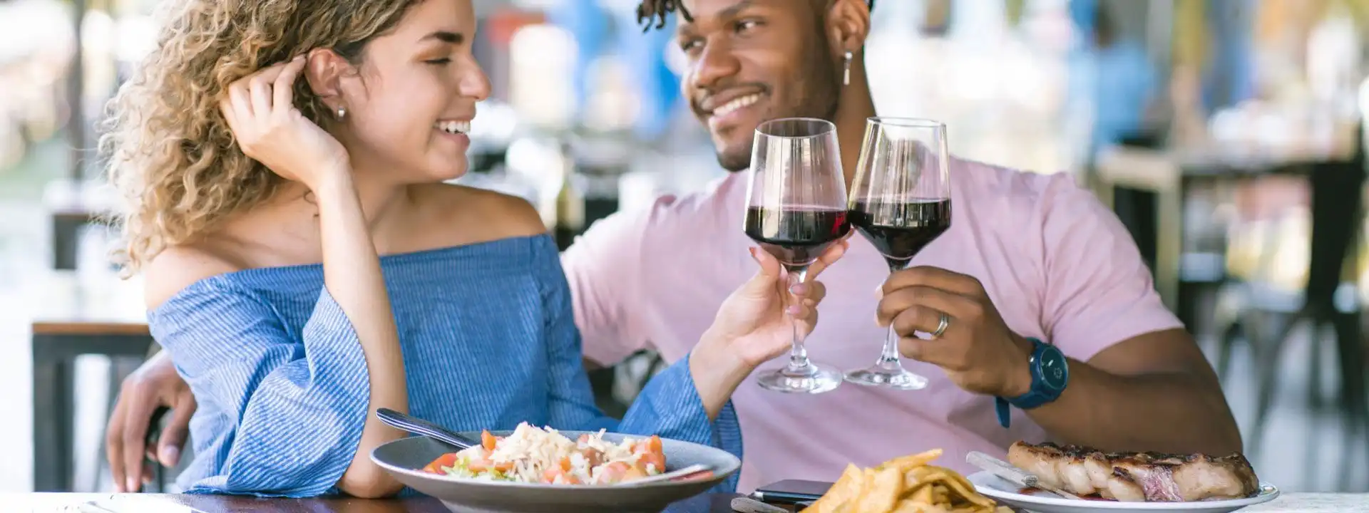 young mixed race couple dining on an outdoor patio toasting with wine glasses