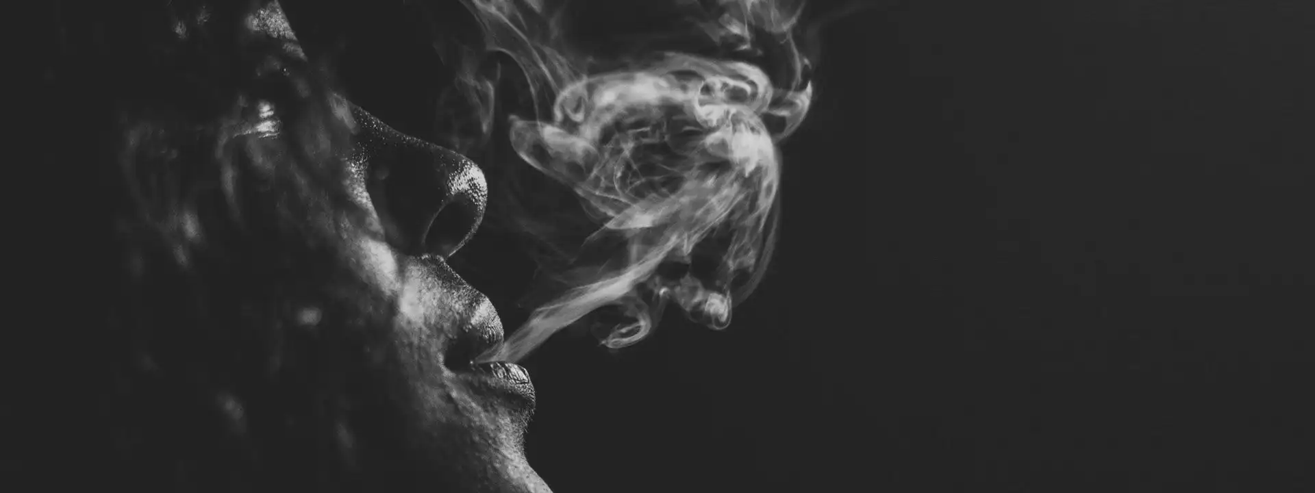 dark closeup of lips blowing out smoke from a vaping device