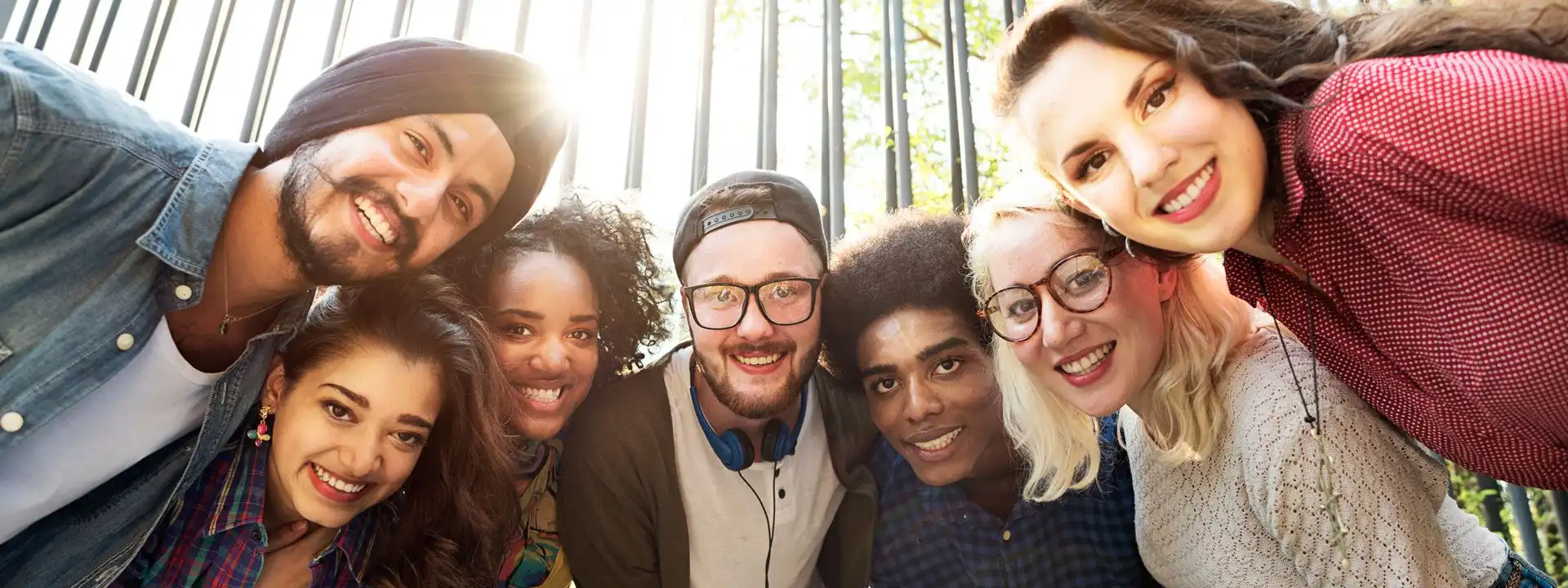 smiling huddle of diverse young adults in front of a large iron fence