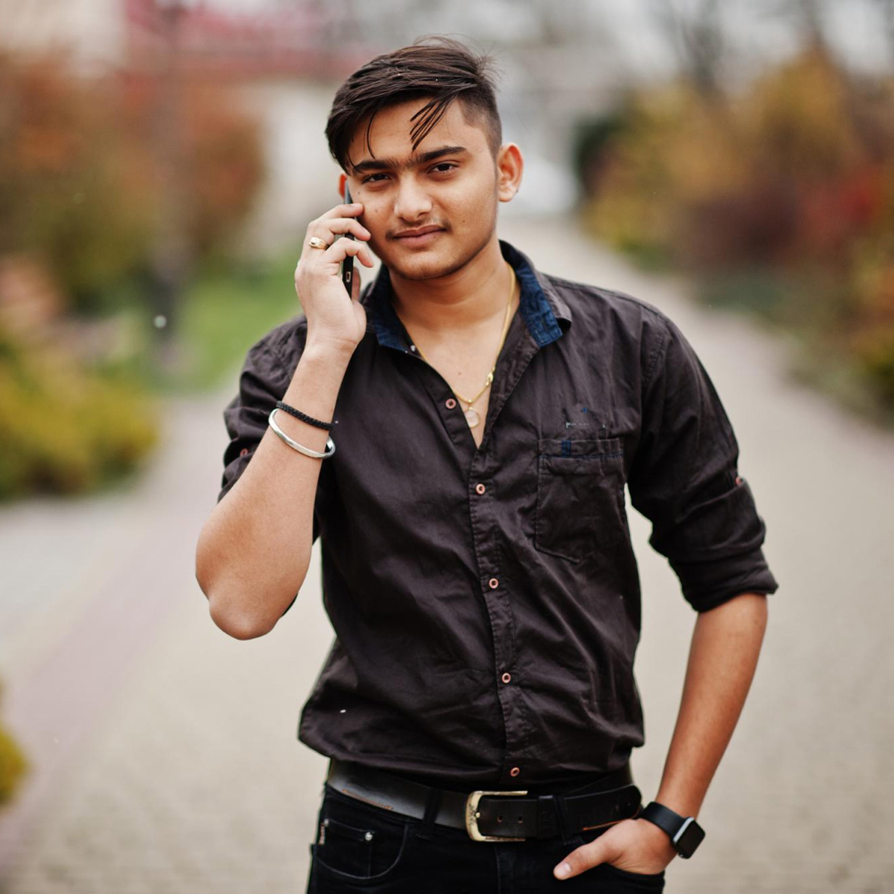 Indian man in brown shirt outdoor and speaking on mobile phone