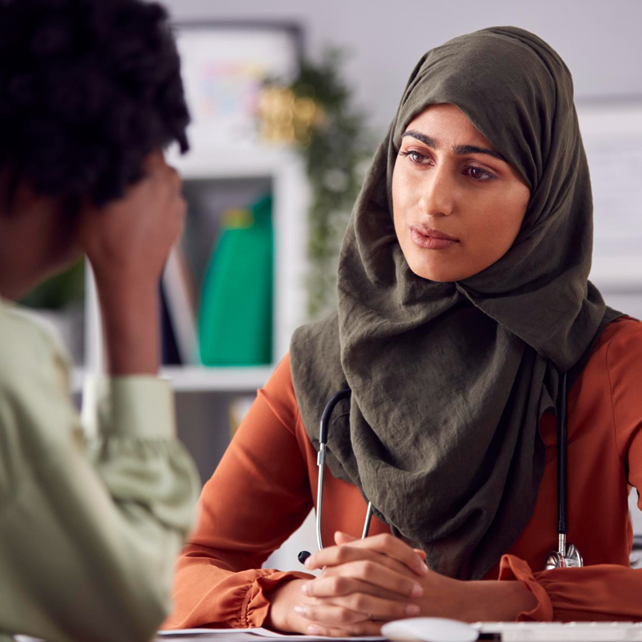 Female counsellor wearing a hijab writing notes on a clipboard while talking to a client in an office setting